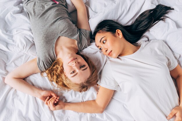Young women lying in bed and holding hands