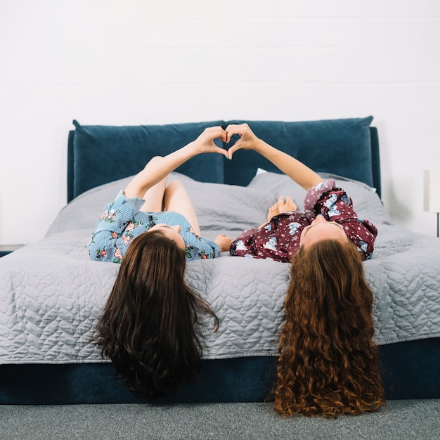 Free photo young women lying on bed making heart shape