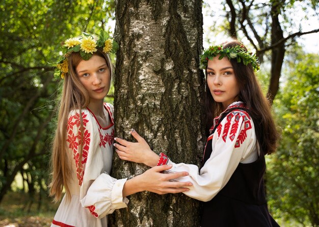Молодые женщины позируют, обнимая дерево.