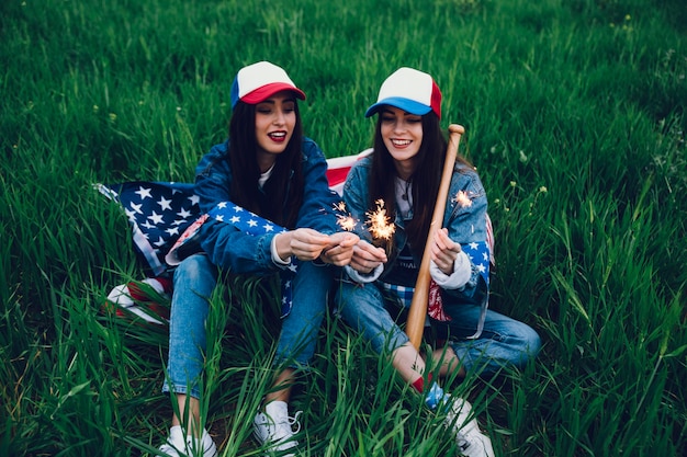 Молодые женщины, сидя на зеленой траве с американским флагом