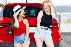 Free photo young women standing by red car and laughing