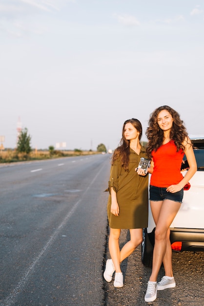 Foto gratuita giovani donne in piedi vicino a macchina con la macchina fotografica