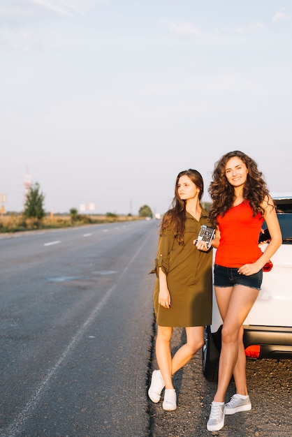 Young women standing near car with camera