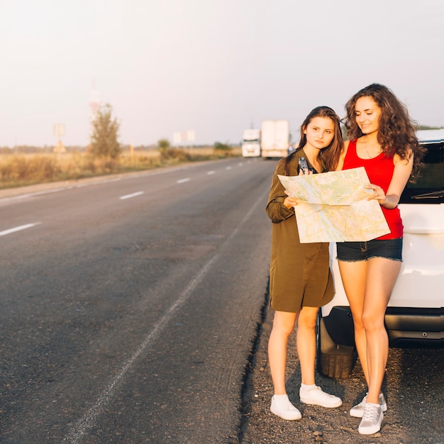 Young women standing near white car with map