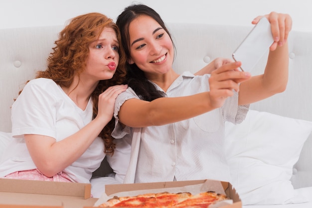 Молодые женщины, принимающие селфи во время еды пиццы