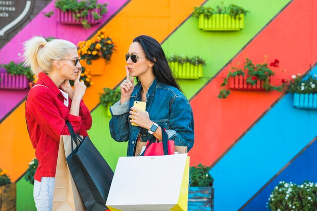 Young women with bags showing silent near wall