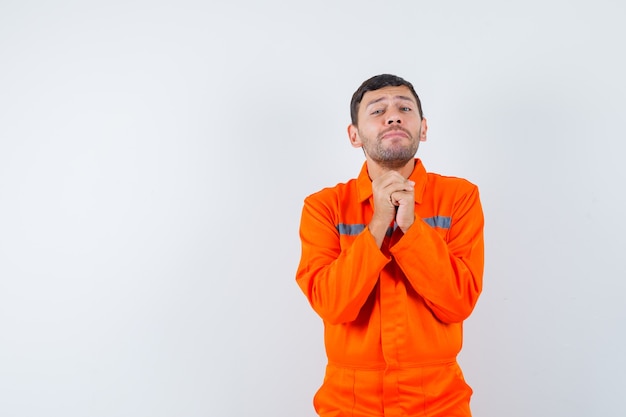 Young worker clasping hands in praying gesture in uniform and looking humble.