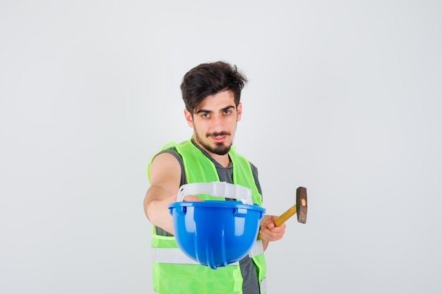 Free photo young worker in construction uniform holding cap and axe and looking amiable