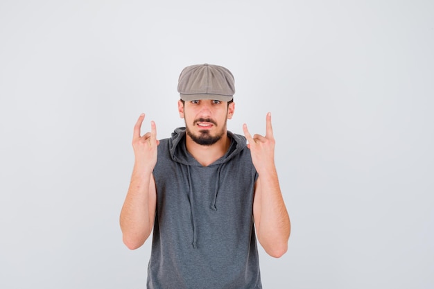 Young worker in gray t-shirt and cap showing rock n roll gesture and looking happy