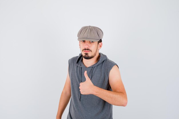 Young worker in gray t-shirt and cap showing thumb up and looking serious