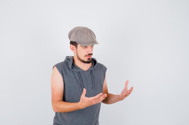 Young worker in gray t-shirt and cap stretching hands as receiving something and looking serious