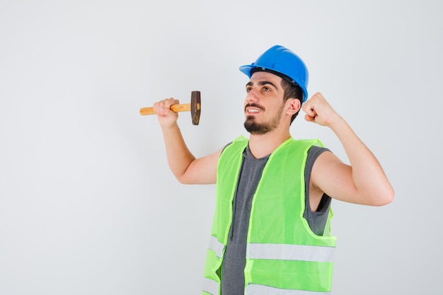 Young worker holding axe in one hand while showing power gesture in construction uniform and looking happy