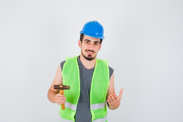 Young worker holding axe in one hand while stretching another hand as holding something in construction uniform and looking happy