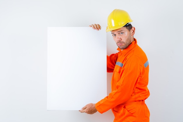 Young worker holding blank canvas in uniform, helmet .