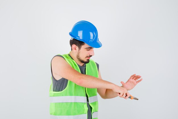 Молодой рабочий держит плоскогубцы и протягивает к нему руку в строительной форме и выглядит счастливым