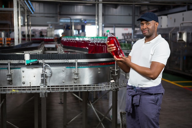 Young worker inspecting juice bottle at factory