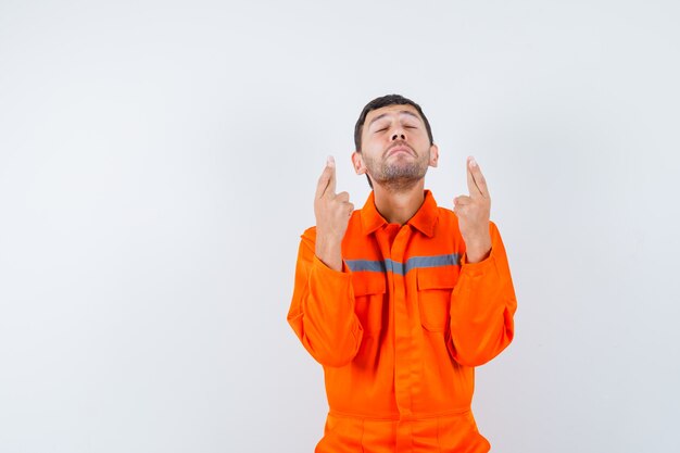 Young worker keeping fingers crossed in uniform and looking dreamy.