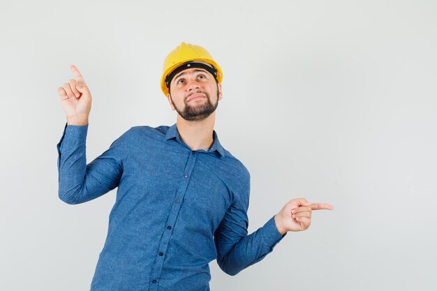 Young worker pointing away in shirt, helmet and looking hopeful.