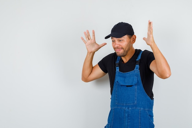 Young worker raising hands in helpless manner in uniform and looking upset , front view.