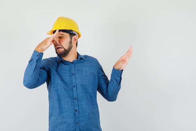 Young worker in shirt, helmet pinching nose due to bad smell and looking disgusted