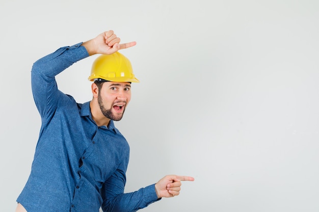 Young worker in shirt, helmet pointing to the side and looking glad