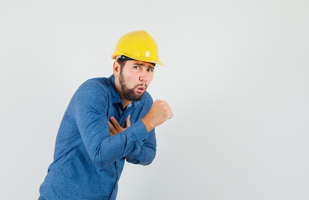 Foto gratuita giovane operaio in camicia, casco che soffre di tosse e che non sembra stare bene