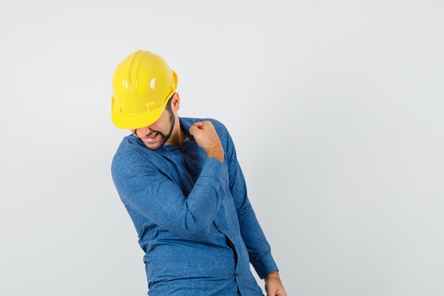 Free photo young worker showing winner gesture in shirt, helmet and looking happy