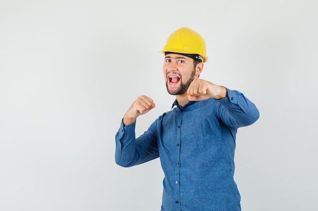 Free photo young worker standing in fight pose in shirt, helmet and looking frisky.