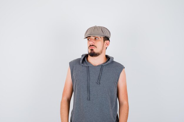 Young worker standing straight, looking away and posing at front in gray t-shirt and cap and looking serious