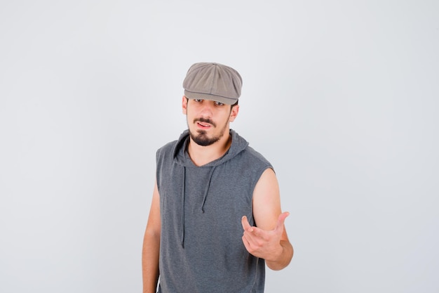Free photo young worker standing straight and stretching hand toward front in gray t-shirt and cap and looking happy