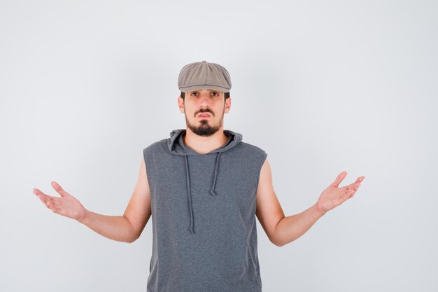 Free photo young worker stretching hands in questioning manner in gray t-shirt and cap and looking baffled