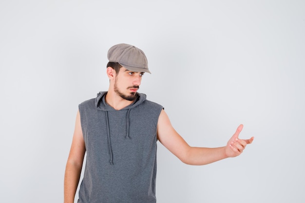 Young worker stretching one hand as receiving something in gray t-shirt and cap and looking serious