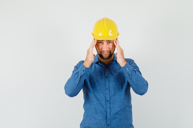 Foto gratuita giovane lavoratore che soffre di forte mal di testa in camicia, casco e sembra stanco