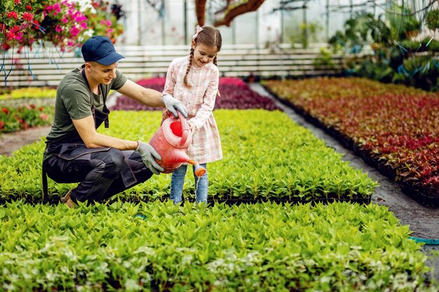 어린 소녀에게 식물 종묘장에서 물뿌리개를 함께 사용하면서 식물에 물을 주는 방법을 가르치는 젊은 노동자