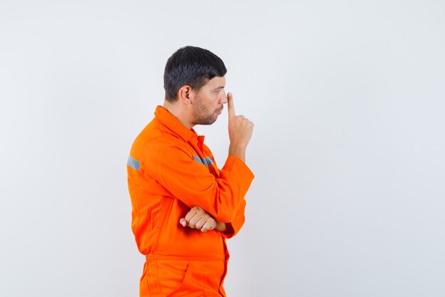 Young worker touching nose with finger in uniform and looking pensive .