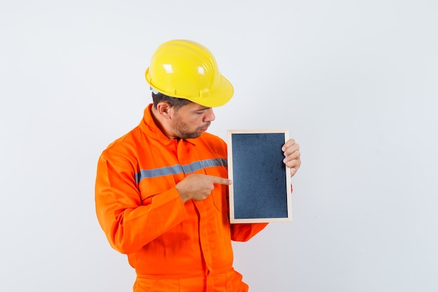 Foto gratuita giovane operaio in uniforme che indica alla lavagna e che sembra concentrato.