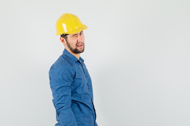 Young worker winking eye and looking at camera in shirt, helmet .