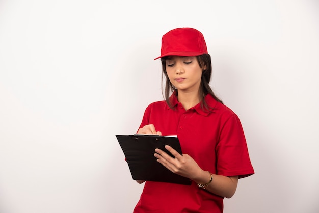 Giovane operaio con uniforme rossa e appunti su sfondo bianco.