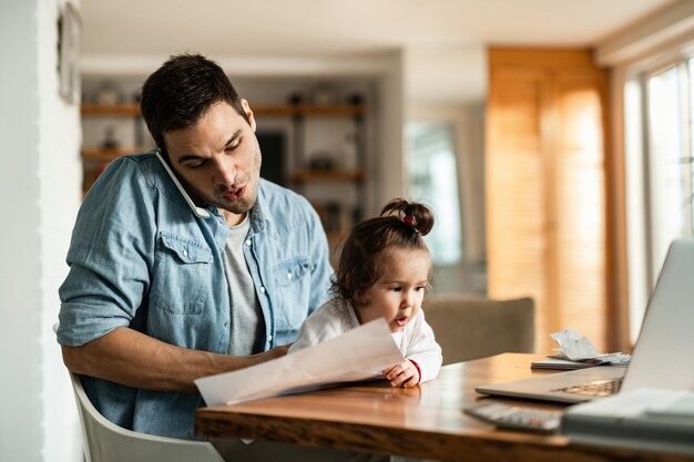 Young working father babysitting his small daughter and making a phone call at home