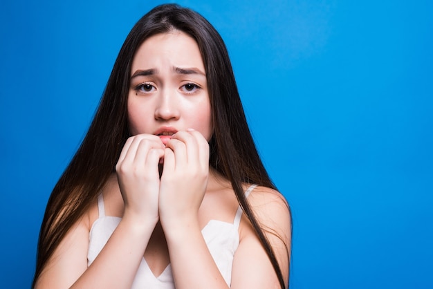 Young worried asian woman isolated on blue wall