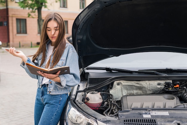 車の避難を呼びかけている心配している若い女性が道路で故障した。女性は故障した車の保険サービスを呼び出します。