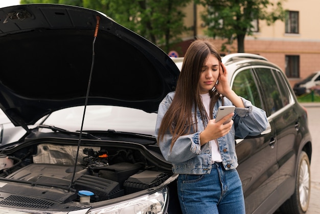 車の避難を呼びかけている心配している若い女性が道路で故障した。