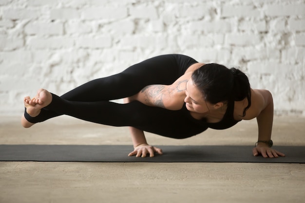 Young yogi attractive woman in Astavakrasana pose, white loft ba