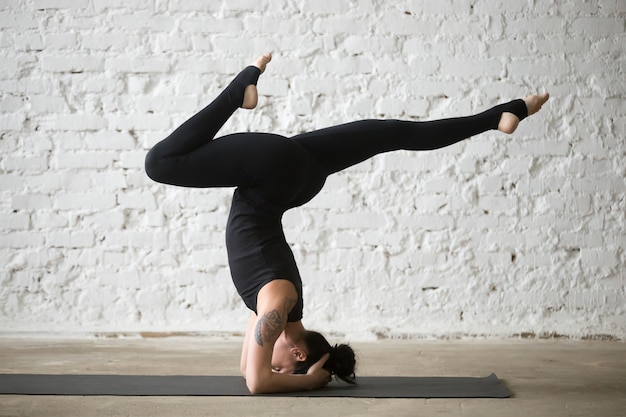 サポートされているheadstandのポーズvariaをやっている若いヨギーの魅力的な女性