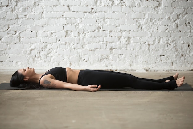 Young yogi attractive woman in savasana pose, white loft backgro