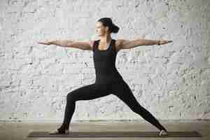 Free photo young yogi attractive woman in warrior two pose, loft background