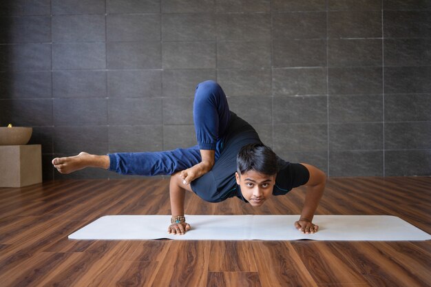 Young yogi doing astavakrasana exercise in gym