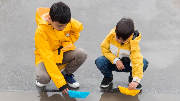 Youngsters in raincoats playing with plastic boats long shot