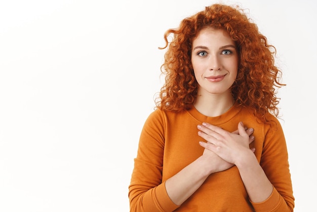 Your support mean a lot Touched tender gorgeous redhead woman with blue eyes curly haircut press hands to heart grateful smiling pleased thankful for nice gift appreciate help white background