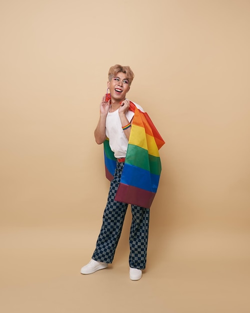 Free photo youth asian transgender lgbt with rainbow flag on shoulder isolated over nude color background man with a gay pride flag concept